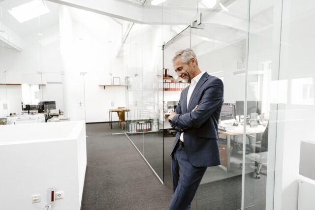a highly compensated employee, well dress mature man relaxes against a wall in a nice office.