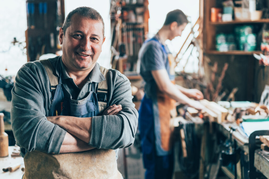 Small business owners working in a woodworking shop, wearing aprons and surrounded by tools and wooden materials, representing hands-on craftsmanship and entrepreneurship. Ideal for business owners exploring 401(k) retirement plan options to support employees and secure long-term financial growth.