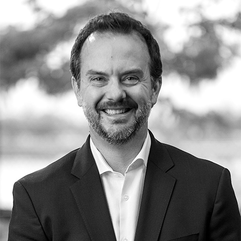 Black and White photo of white middle aged man wearing a blazer. This is Colin Smith's bio.