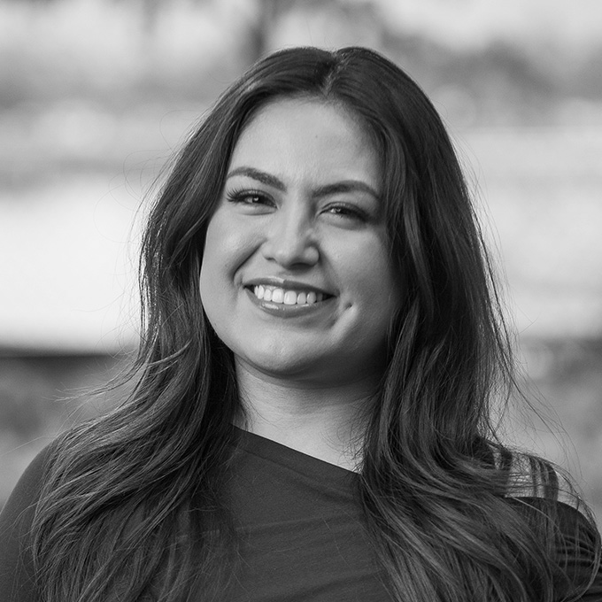 Black and white image of woman with dark long hair smiling at the camera. This is Itati Tapia's bio.