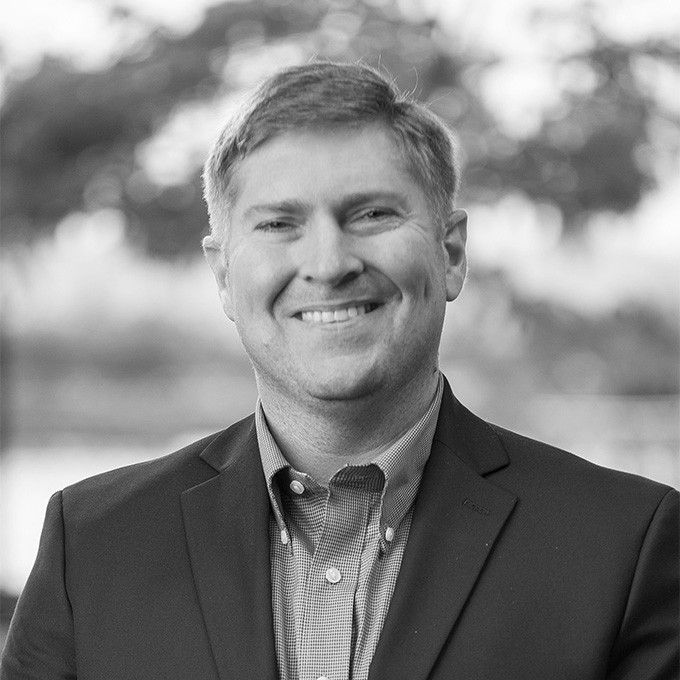 Black and white image of man in blazer smiling at camera. This is Jaspar Mallard's bio.