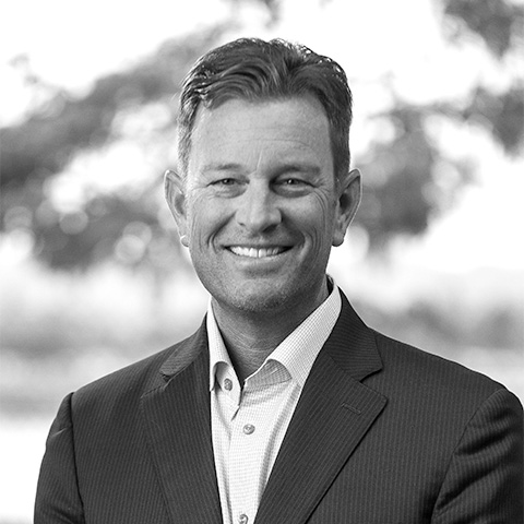 Black and White photo of white middle aged man wearing a blazer. This is Justin McDonald's bio.