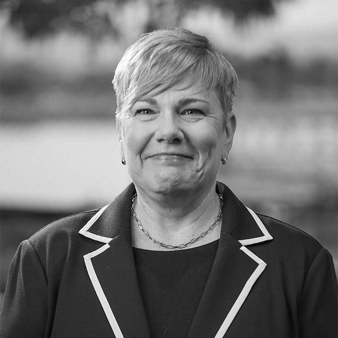Black and white image of a woman with short blond hair smiling at the camera. This is Liz Butler's bio.