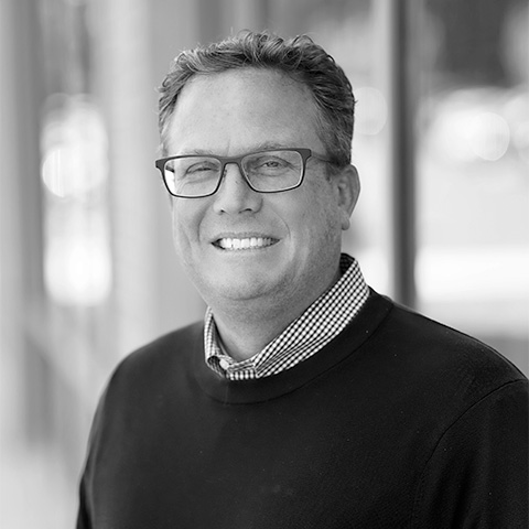 Black and White photo of white middle aged man wearing a blazer. This is Matthew Huddleston's bio.
