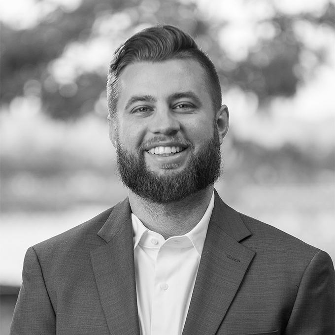 Black and white image of man with a beard in blazer smiling at the camera. This is Ty Boggs' bio.