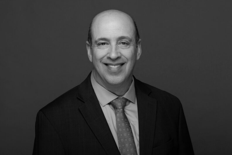 Photo of a middle-aged man in a blazer and tie smiling. This is Joe Mattei's biography