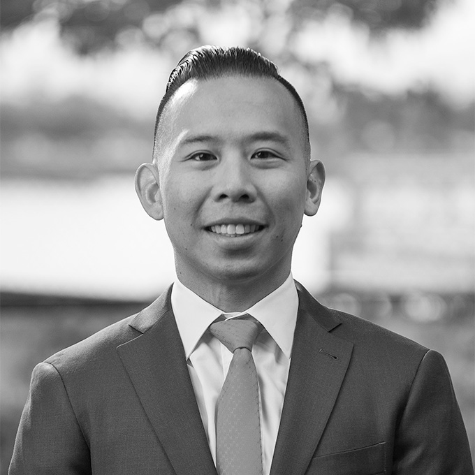 Black and white image of an Asian man in a suit and tie smiling at the camera. This is Chen-Han Wang's bio.
